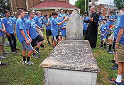 In the cemetery of St. Vincent de Paul Parish in Shelby County on July 10, archdiocesan vocations director Father Michael Keucher gathers with Bishop Brut&eacute; Days participants around the grave of Father Vincent Bacquelin, the first priest to minister regularly in central Indiana. (Photo by Sean Gallagher) 