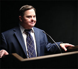 Mark Hublar poses in front of a podium as he would at any of his public speaking events to advocate for employment of those with disabilities and to share the message that &ldquo;we&rsquo;re all different, but the same.&rdquo; (Submitted photo)