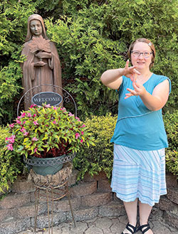 Hannah Houser, a postulant with the Franciscan Sisters in Oldenburg, uses American Sign Language (ASL) by a statue of St. Clare of Assisi on the campus of the sisters&rsquo; motherhouse. Although not hearing impaired, Hannah has learned ASL because a disability she has called apraxia can make it difficult for her to speak. (Photo by Sara Geer)