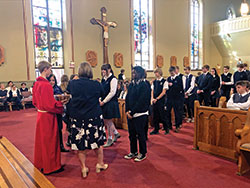 Altar server Zachary Hoff holds a basket of blessed Miraculous Medals as the school&rsquo;s president Diane Laake (to his left) and principal Angie Parmer (to his right) place a medal around the neck of each new student and staff member on Dec. 8. (Submitted photo by Theresa Murphy)