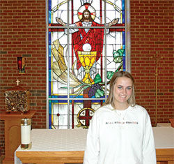 Wearing her sweatshirt stitched with the phrase, &ldquo;Make Heaven Crowded,&rdquo; 18-year-old Celia Boring has made it a goal during her senior year at Roncalli High School in Indianapolis to spend more time in eucharistic adoration&mdash;and invite others to do the same. Here, she poses in front of a stained-glass window featuring Jesus and the Eucharist in the school&rsquo;s chapel. (Photo by John Shaughnessy)