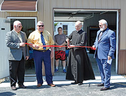 Father John Hollowell, pastor of Annunciation Parish in Brazil, prepares to cut a ribbon during an opening ceremony for the parish&rsquo;s new St. Vincent de Paul food pantry building on April 23. Holding the ribbon are Larry Tempel, left, Brazil Mayor Brian Wyndham and Patrick Hardman, president of the Annunciation Parish St. Vincent de Paul conference in Brazil. (Photo by Natalie Hoefer)