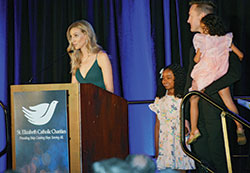 Lauren Niehoff shares the story of her and her husband Brian&rsquo;s journey of adopting Roslyn, center, while Brian holds their second adopted daughter, Ainsley, during the St. Elizabeth Catholic Charities fundraiser gala at Galt House Hotel in Louisville on April 21. (Photo by Natalie Hoefer)