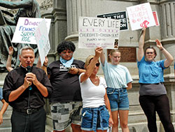 Pro-life youths and young adults stand behind Father Rick Nagel as he offers a prayer of thanksgiving for the Supreme Court&rsquo;s Dobbs decision during a June 25 prayer gathering on the grounds of the Indiana Statehouse in Indianapolis. A small group of pro-choice protestors shouted as Father Nagel offered his comments and a blessing to both the protestors and the 200 pro-life supporters at the gathering. (Photo by John Shaughnessy)