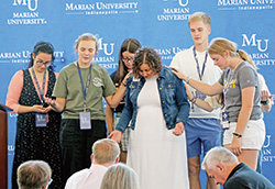 Marian University students who are part of the school&rsquo;s San Damiano Scholarship program pray with Shannon Wimp Schmidt before she gives a keynote address on Aug. 13 at Marian during the archdiocesan-sponsored Into the Heart Conference for people from many backgrounds involved in the lives of youths. (Submitted photo)