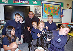 With his dog Guinness surrounded by smiling school children, Father Douglas Hunter doesn&rsquo;t mind being in the background when he makes a visit to a fifth-grade classroom at St. Roch School in Indianapolis. (Photo by John Shaughnessy)