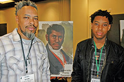Seeking to grow in their faith and their relationship, Jason Smith and his 15-year-old son Trenton shared time together at the National Black Catholic Men&rsquo;s Conference in Indianapolis on Oct. 13-16. They posed for a photo by an image of Venerable Pierre Toussaint, a former slave who went on to serve the Church and the poor and who is now up for sainthood. (Photo by John Shaughnessy)