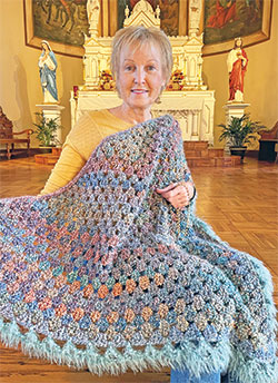 Wrapped in the prayer blanket that she was given after her first cancer diagnosis, Kim Zimmerman has been coordinating the All Saints Parish Ladies Sodality Prayer Shawl Ministry for the past eight years, a ministry that has created 854&mdash;and counting&mdash;prayer shawls for people facing a crisis in their lives. (Submitted photo)