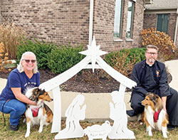 St. Malachy Parish in Brownsburg is one of the 28 schools and parishes in central Indiana that participated in the continuing effort to emphasize the true meaning of Christmas and help make central Indiana the &ldquo;Outdoor Nativity Scene Capital of the United States,&rdquo; the goal of Jim Liston, who started the program. Jean McCorkhill, St. Malachy&rsquo;s coordinator of children&rsquo;s faith formation, and Father Sean Danda, pastor of the parish, pose by one of the Nativity scenes with Father Danda&rsquo;s dogs, Finley and Bentley. (Submitted photo)