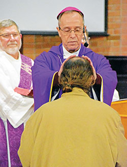 Archbishop Charles C. Thompson, principal celebrant of a Mass celebrated at the Plainfield Correctional Facility in Plainfield on March 26, offers a blessing to a man soon to be released from the facility. Deacon Martin &ldquo;Neil&rdquo; May stands at left. (Photo by Natalie Hoefer)