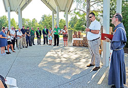 Ben Wissel, a member of the New Albany Knights of Columbus #1221 Council, second from right, recites a poem during a burial service for miscarried babies&mdash;whose tiny caskets seen in the background were built by the Knights&mdash;at Holy Trinity Cemetery in New Albany on July 14. The service was led by Conventual Franciscan Father Mark Weaver, pastor of St. Mary Parish in New Albany, at right. (Photo by Natalie Hoefer)