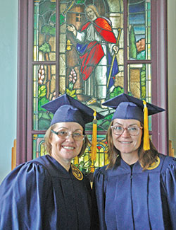 Michelle Williams, left, and Rheann Kelly pose for a photo in front of a stained-glass window in the chapel of the Indiana Women&rsquo;s Prison in Indianapolis on Aug. 7 after receiving their college diplomas from Marian University in Indianapolis.  (Photo by John Shaughnessy)