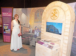 Jude Anton Twal poses in front of the area of the &ldquo;Sacred Places&rdquo; exhibit at The Children&rsquo;s Museum of Indianapolis that features her, her Christian faith and her Catholic parish church, The Beheading of St. John the Baptist Catholic Church in Madaba, Jordan. (Photo courtesy of The Children&rsquo;s Museum of Indianapolis)
