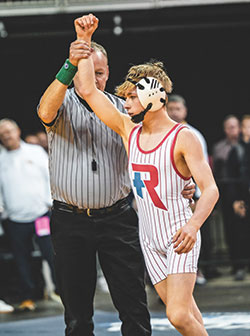 A referee raises the arm of Peyton Schoettle, signifying that the sophomore from Roncalli High School in Indianapolis has won the 106-pound match in Indiana&rsquo;s state wrestling championship meet on Feb. 17. (Photo courtesy of Pure Impact Studios, LLC)