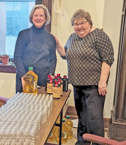 Christina Tuley, right, and Kathy Davis-Shanks of St. Batholomew Parish in Columbus pose in a conference room of SS. Peter and Paul Cathedral Parish&rsquo;s rectory in Indianapolis on March 20 with the components for assembling the holy oils for the archdiocesan chrism Mass, celebrated on April 26. (Photo by Ann Margaret Lewis)