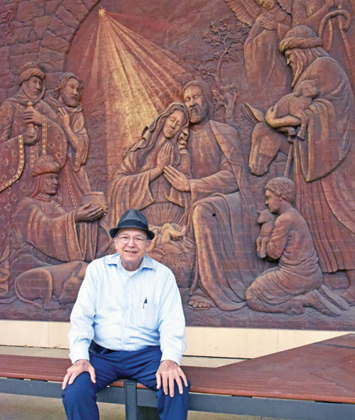 Andy Hohman, a retired philosophy and theology professor at Marian University in Indianapolis, sits by a relief sculpture of the adoration of the Magi on its campus on July 30. He recently retired after spending 40 years on the university&rsquo;s faculty. (Photo by Sean Gallagher)