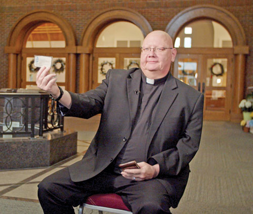 Father John McCaslin, pastor of St. Monica Parish in Indianapolis, shows a business card with the archdiocesan vocations director&rsquo;s contact information he received 30 years ago that was a pivotal moment in his discernment of his vocation to the priesthood. He&rsquo;s kept the business card as a &ldquo;sign of God&rsquo;s faithfulness to me.&rdquo; (Photo courtesy of Cantaloupe)