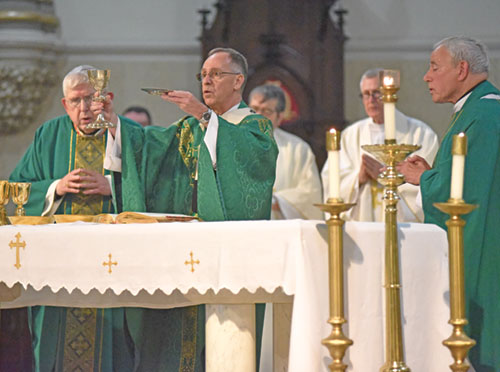 Archbishop Charles C. Thompson, center, elevates the Eucharist during the July 9 opening Mass of the annual convention of Serra International. The liturgy was celebrated at St. John the Evangelist Church in Indianapolis. Concelebrating at the Mass are Cardinal Thomas C. Collins, archbishop emeritus of Toronto, left, and Archbishop J. Michael Miller, archbishop emeritus of Vancouver, British Columbia. (Photo by Sean Gallagher)