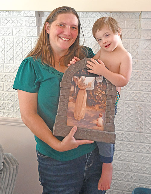 At Loads of JOY laundry service in North Vernon, Kelly Elkins displays a copy of the painting &ldquo;Saturday Rays,&rdquo; also known as &ldquo;Our Lady of the Laundry,&rdquo; while holding Elliot, her 3-year-old bundle of joy with Down syndrome. Loads of JOY&rsquo;s threefold mission is to help mothers in need, benefit Gabriel Project of Jennings County and offer support and resources to parents of unborn or newborn children diagnosed with Down syndrome. (Photo by Natalie Hoefer)